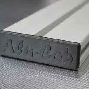 ALULB-1250-S-1__15269 – Wolf Customs | 4x4 Accessories and Fitment Close-up of a silver rectangular metal bar with a rounded end and cursive engraving on the end face on a textured surface.