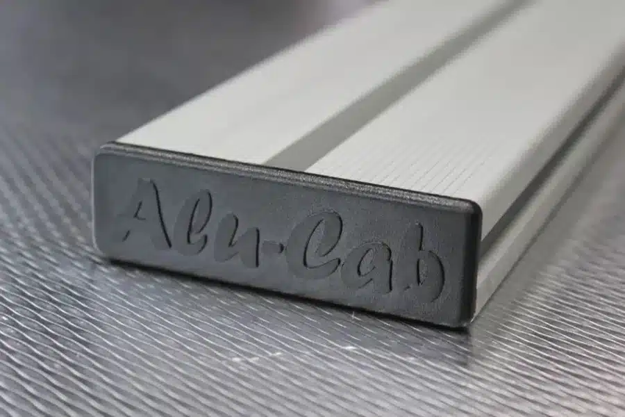 ALULB-1250-S-1__15269 – Wolf Customs | 4x4 Accessories and Fitment Close-up of a silver rectangular metal bar with a rounded end and cursive engraving on the end face on a textured surface.