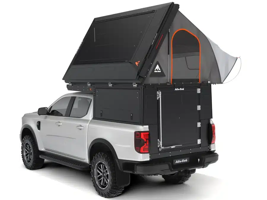 Silver pickup with a large black roof-top tent mounted on the bed, tent extended over cab with orange trim and side storage compartments.